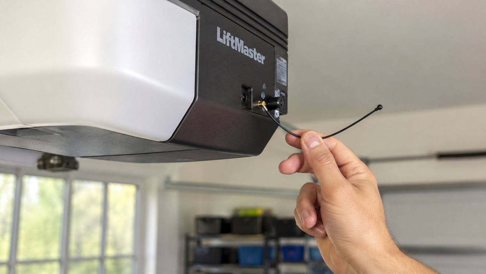A person's hand holding and adjusting the black wire antenna on a LiftMaster garage door opener unit.