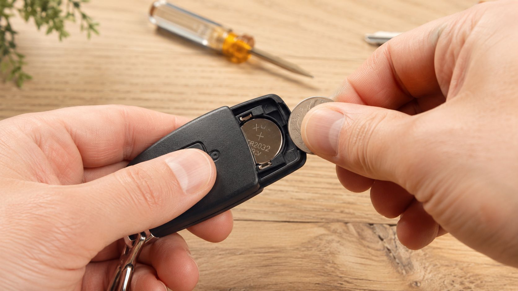 A person using a coin to open a car key fob to replace the internal battery.