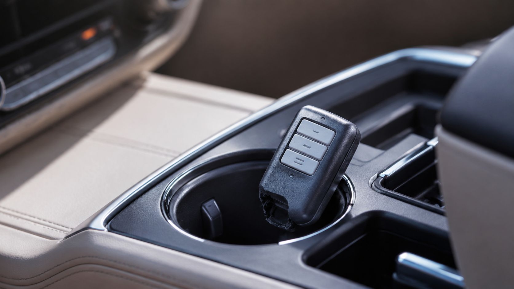 A broken garage door remote controller resting inside the cup holder of a vehicle center console.